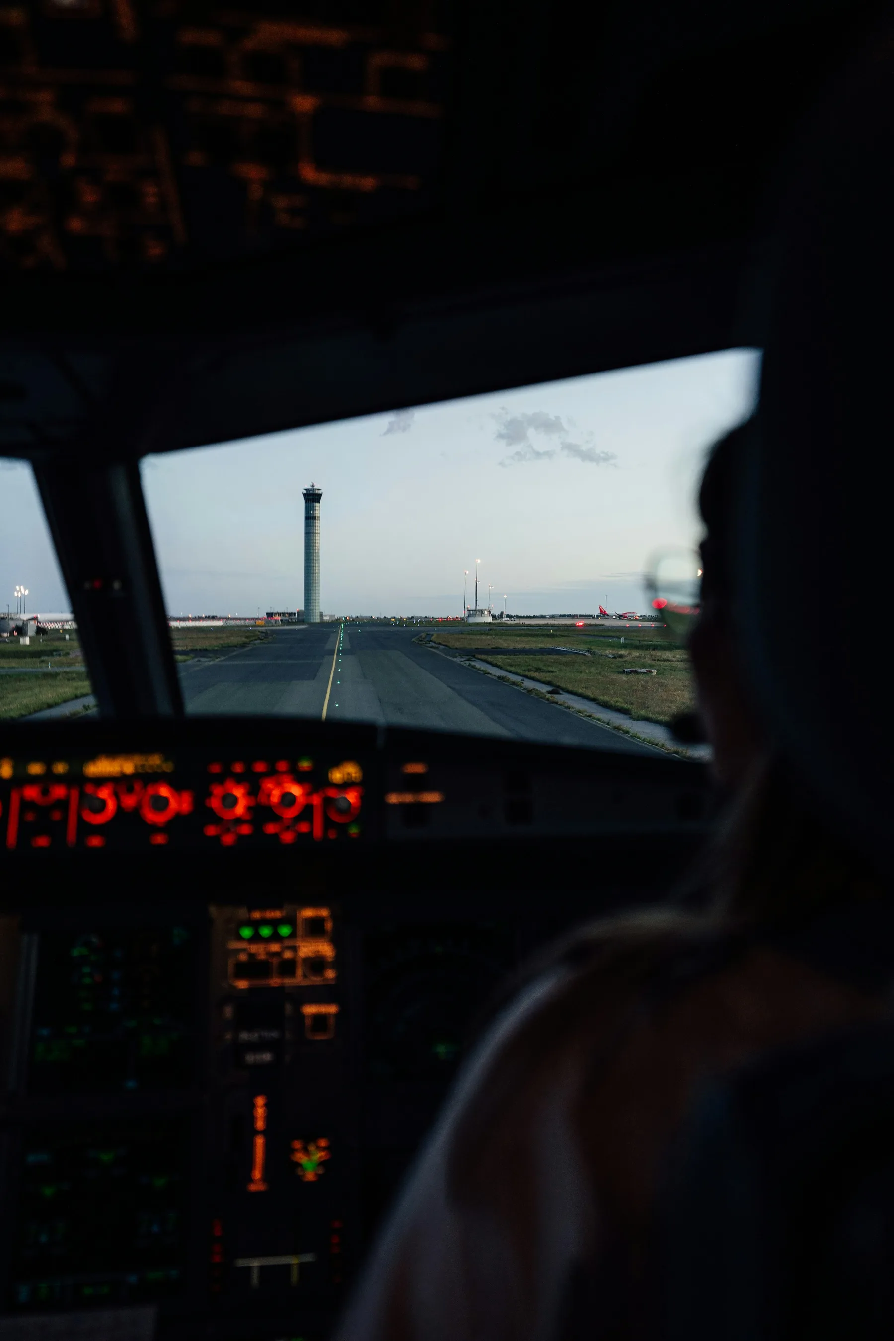 Cockpit at dusk with an air traffic control tower through the windscreen.
